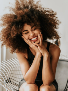 Donna nera con capelli afro che ride a crepapelle con gli occhi chiusi